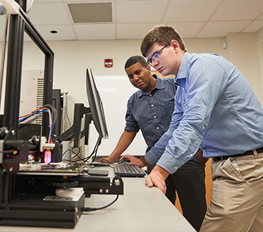 two male students lean over looking at computer