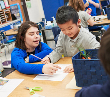 teacher helps young student in classroom