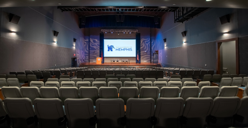 theatre with chairs facing a stage with screen and podium