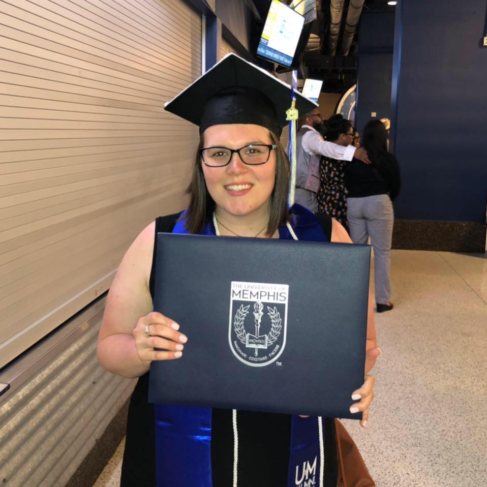 Tiffany smiles with her cap on at commencement while holding her diploma