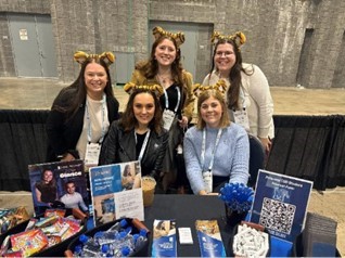 AuD students (standing) and faculty (seated) at the UofM recruitment table at ASHA 2025, Washington DC 