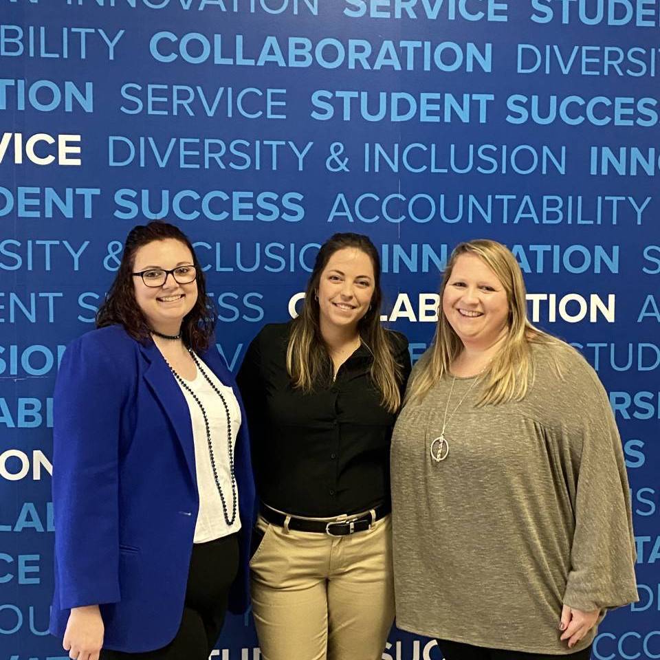 Three female students in front of UofM sign