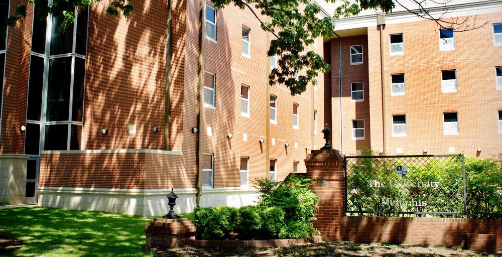 Outside on campus sunny day, front building entrance on campus Living Learning Complex front of building with older Memphis State University signage in foreground. 