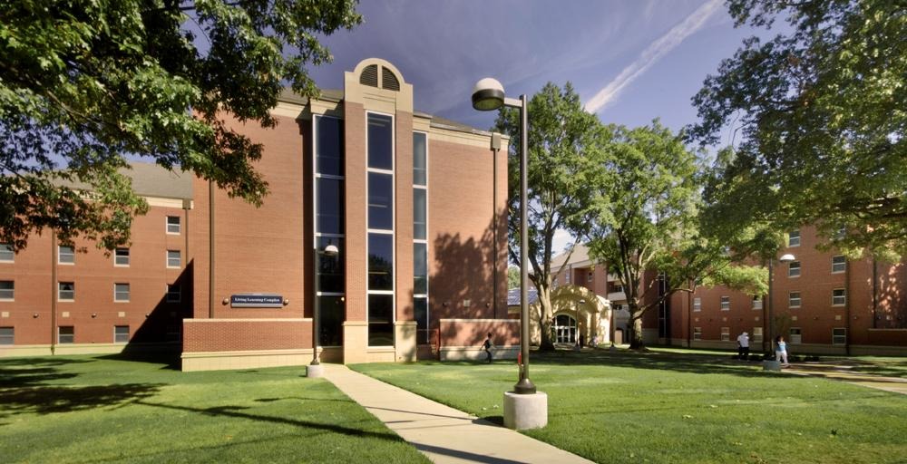 Living Learning Complex (LLC) building complex - four-story entrance view with campus lighting, pathways and beautiful green lawn, blue skies, and numerous aged talk oak trees. 