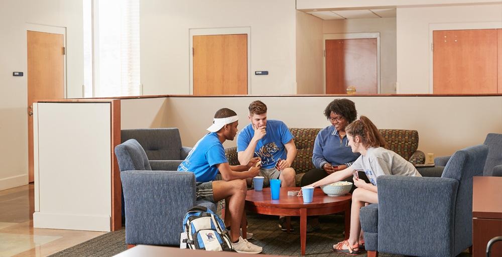Living Learning Complex (LLC) Lounge Area - four students sitting around coffee table playing challenging competitive games and relaxing. 
