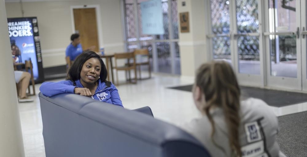 two students lounging relaxing sitting in Rawls Hall Lobby sofa area 
