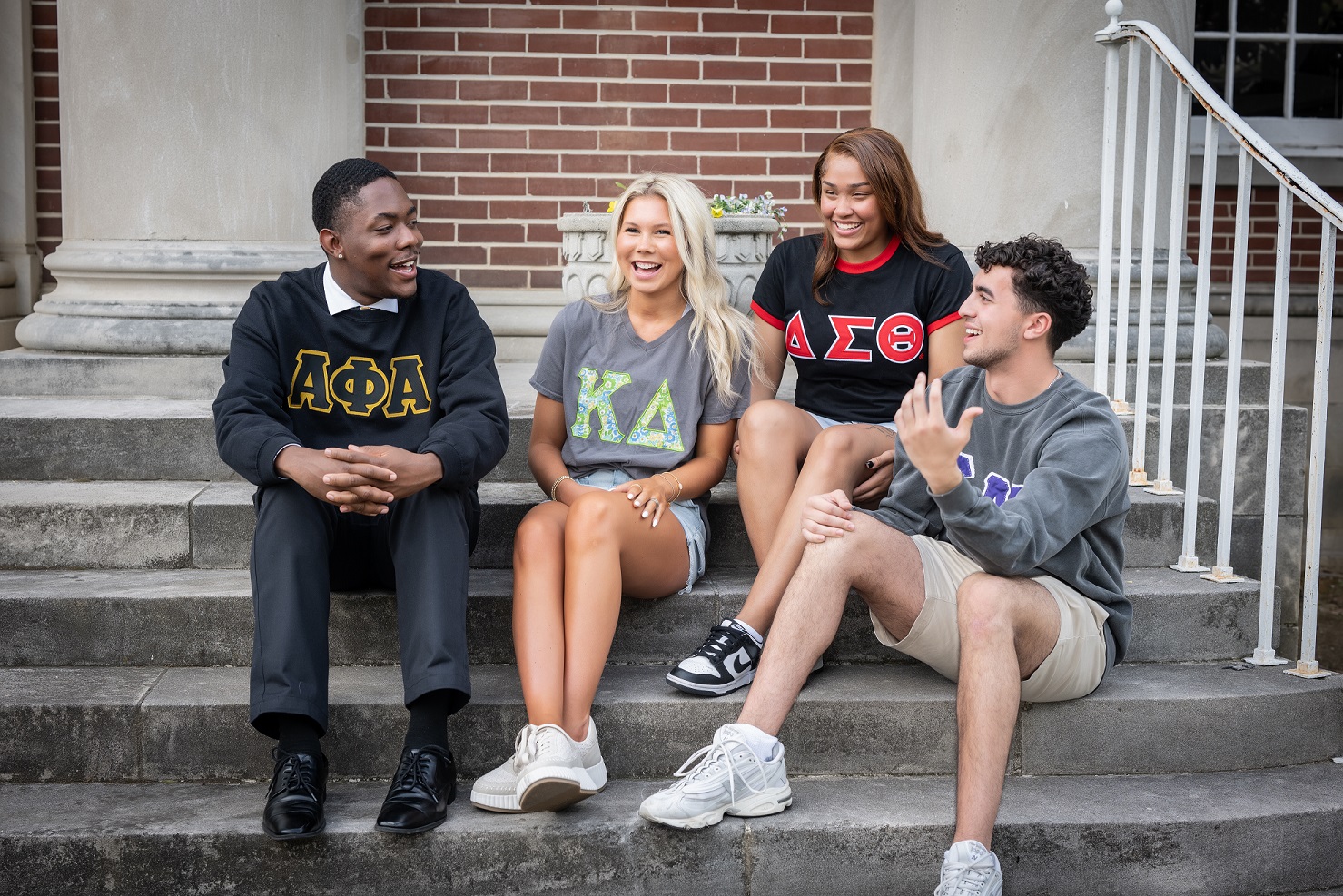 Fraternity and sorority students sitting on the library steps talking with one another.