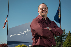 man with arms folded beside lochead martin sign an flag
